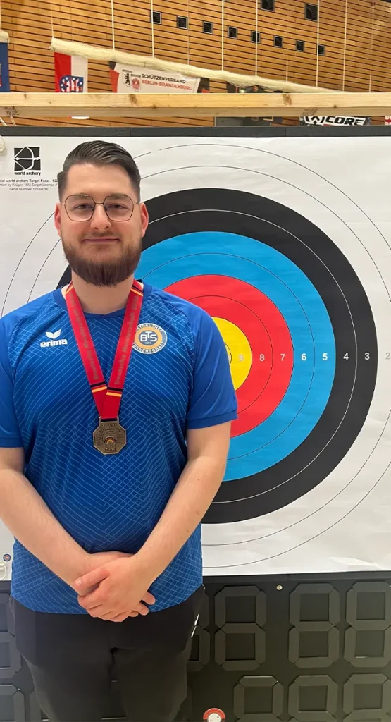 Mann mit Medaille posiert vor einer Zielscheibe