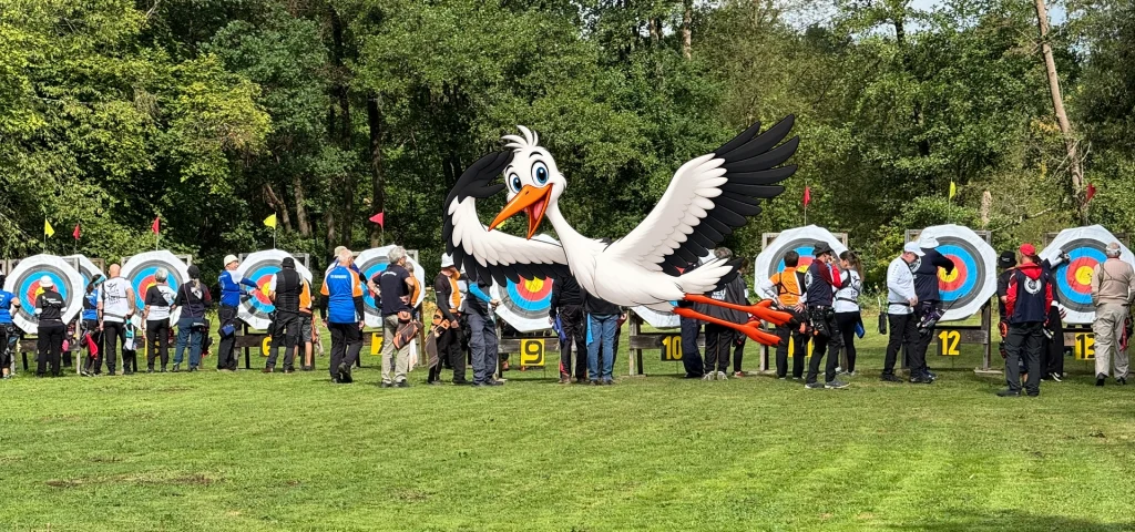 Viele Zielscheiben in verschiedenen Entfernungen auf einer Wiese im Sommer. Schützinnen und Schützen beim Pfeileziehen. Vom Vordergrund fliegt ein gezeichneter Storch vorbei und grüßt freundlich